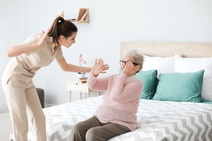 A nurse in a nursing home physically abusing an elderly woman sitting on a bed.