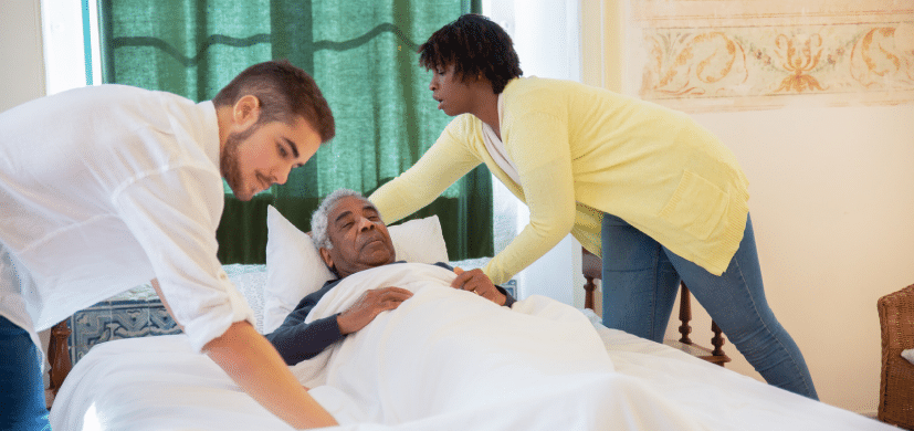 Elderly man in bed surrounded by nursing staff